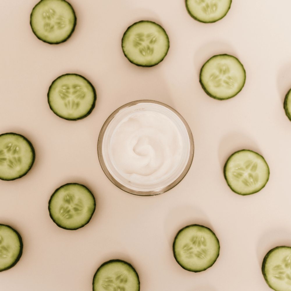 Cucumber slices arranged around a jar of white cream on a beige background